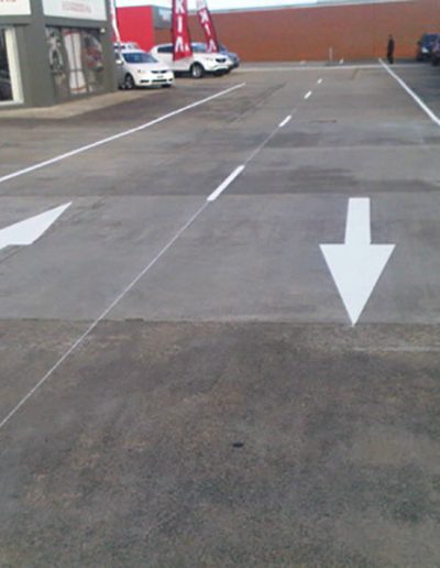 Directional arrows and lane markings on the road around a Kia Motors car yard.